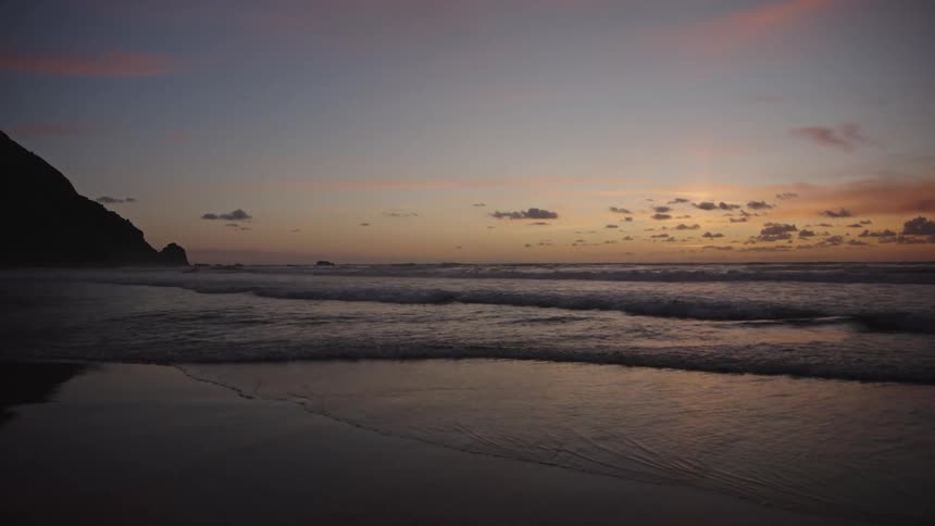 A beach with calm waters and an orange sky at sunset