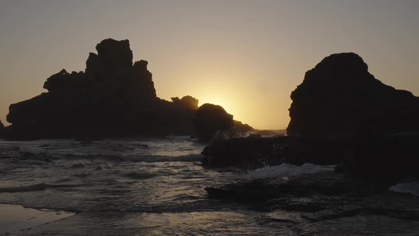 Sun shining from the red horizon casts coastal rock formations into silhouette