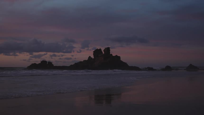 Rock formation in the sea reflected on wet sand at dusk