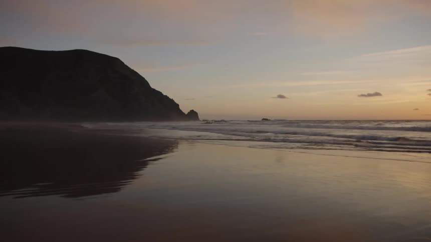 Beach at sunset with gentle waves and a cliff in the background
