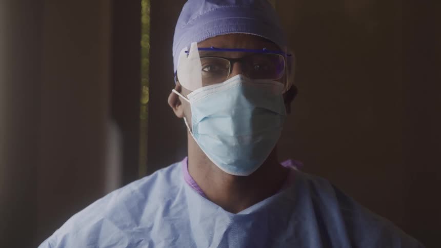 Medical professional wears operating room attire including an eye shield over his eyeglasses