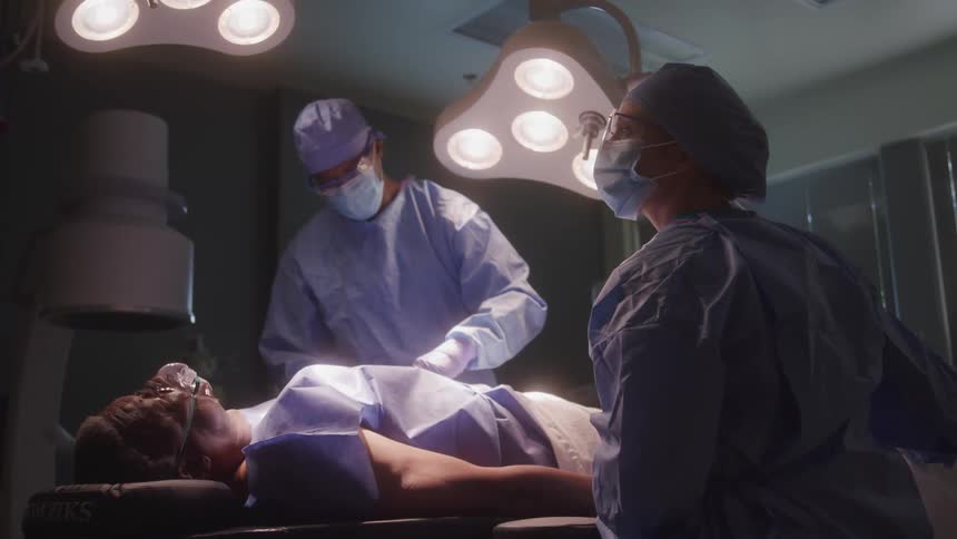 Medical team performs a surgical procedure on a patient lying under operating room lights
