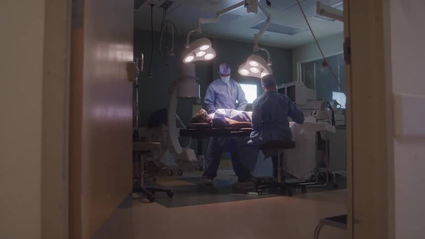 Surgeons perform a procedure on a patient lying on an operating table under bright lights