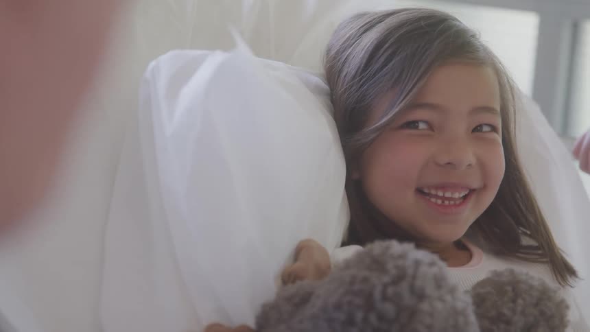 Smiling girl lying in bed hugging a teddy bear