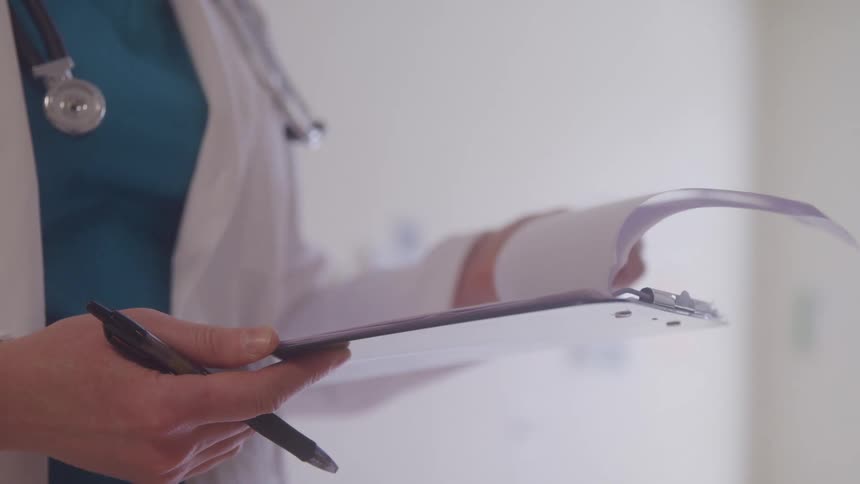 Healthcare professional holds a clipboard and a pen while reviewing documents