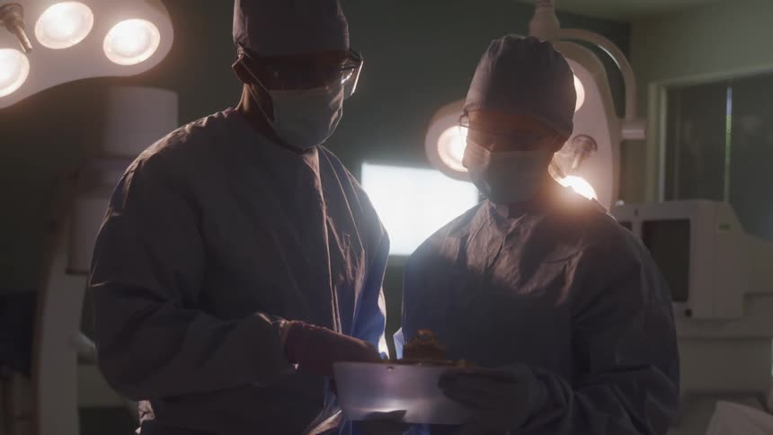 Two surgeons wearing masks and sterile gowns review a clipboard in the operating room