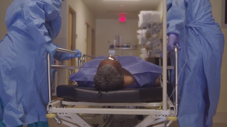 A patient on a stretcher is moved by two healthcare workers