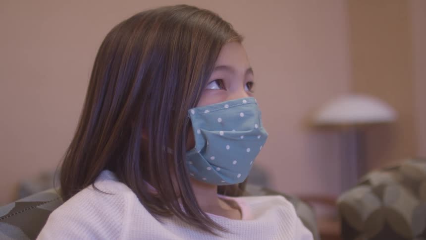 Little girl in a face mask sitting in a doctors office waiting room