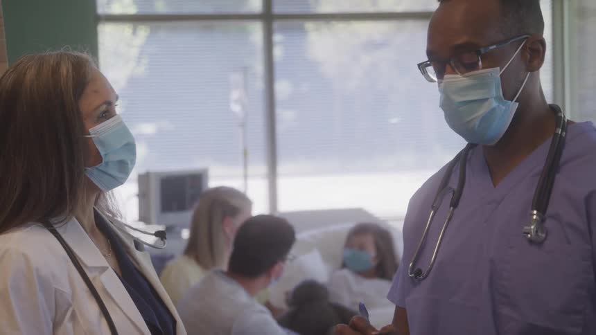 Two healthcare professionals talking in a hospital wearing masks and stethoscopes