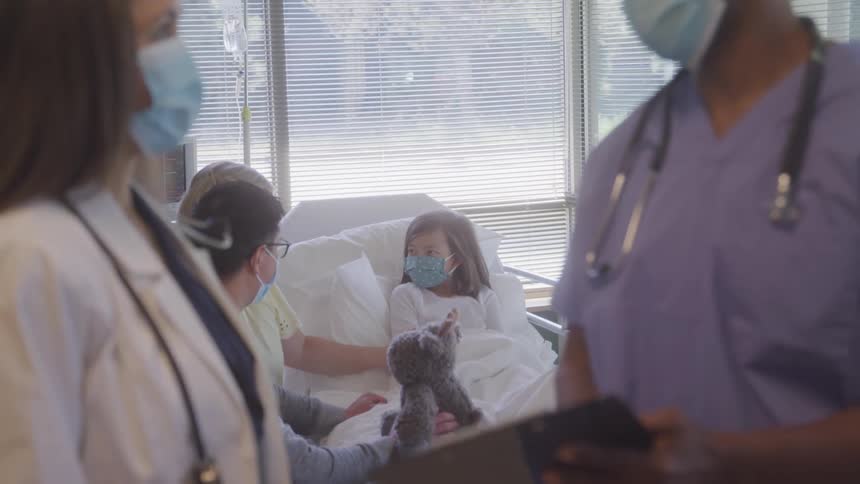 Medical team interacts with a hospitalized child and a companion in the room