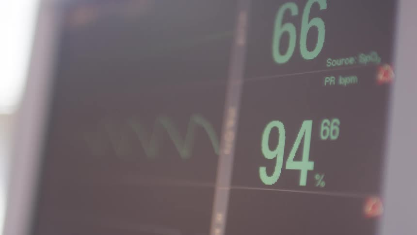A closeup shot of a medical monitor displaying a patients vital signs the numbers for heart rate and oxygen saturation fluctuate showing a heartbeat graphic on the screen