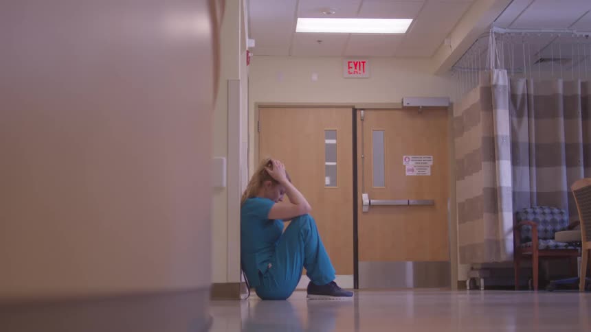 Healthcare professional sits on the hospital corridor floor with hands on head