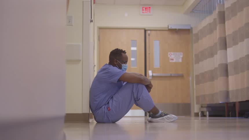 Healthcare worker sitting on the hallway floor with an exhausted expression
