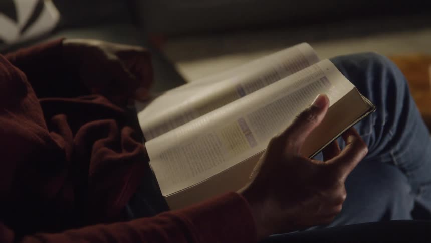 A close view shows a person sitting in a chair and flipping through the pages of a book