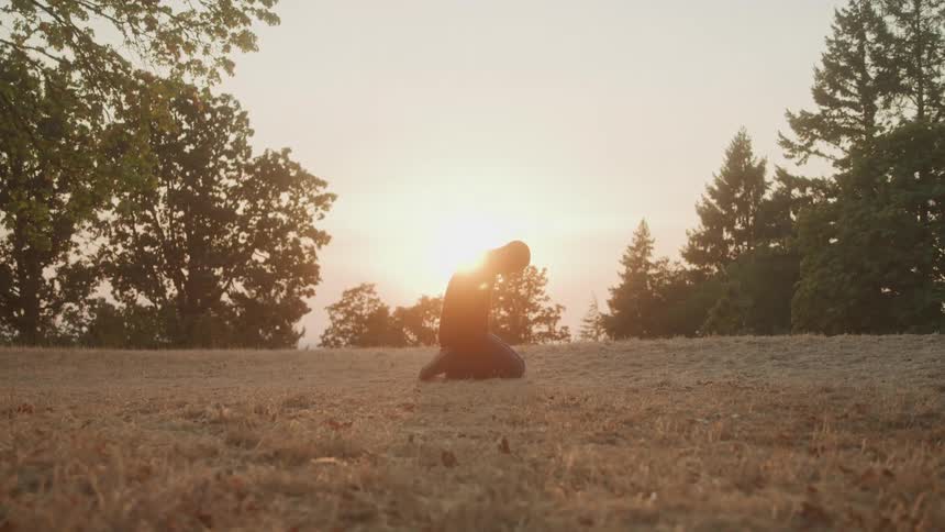 Person kneeling in a dry field during sunset