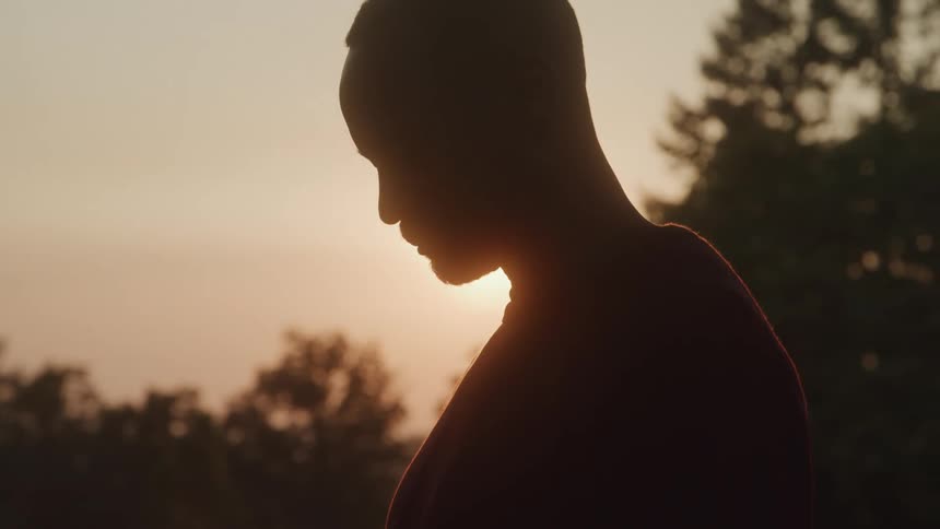 Silhouette of a man with his head bowed at sunset