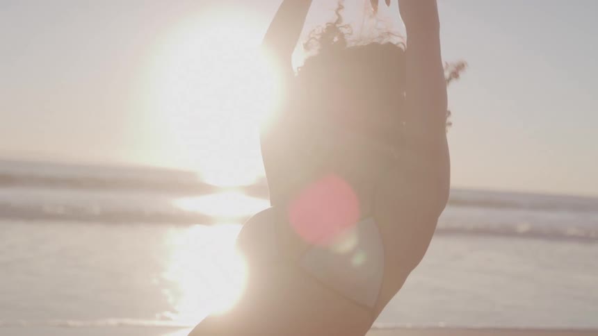 Woman in a gray bikini stretching on the beach at sunrise