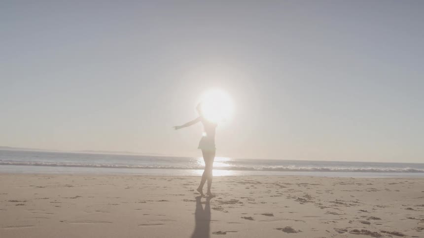Woman running and spinning on the beach at sunrise