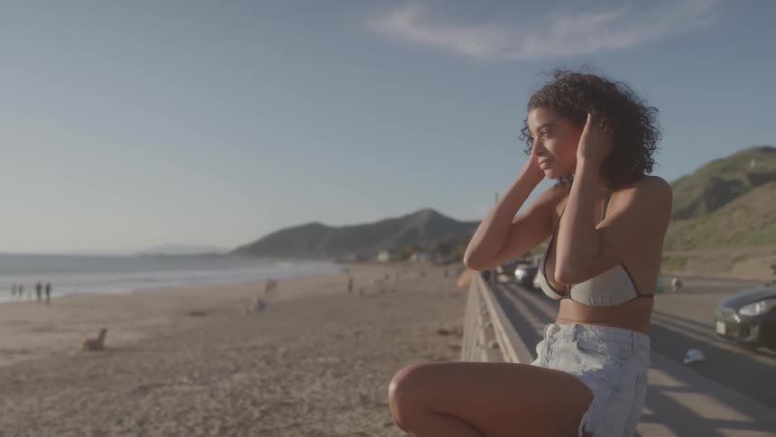 Woman sitting on a railing by the beach at sunset