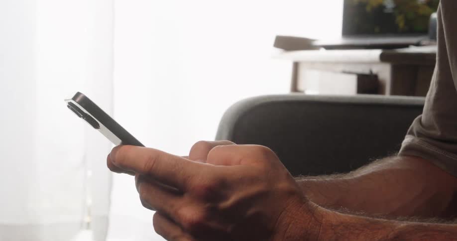 A persons hands are shown holding and using a smartphone the person is indoors with a blurry background that suggests an office or home setting