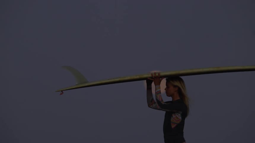 Surfer woman walking and carrying her surfboard with a big fin under the full moon light at night