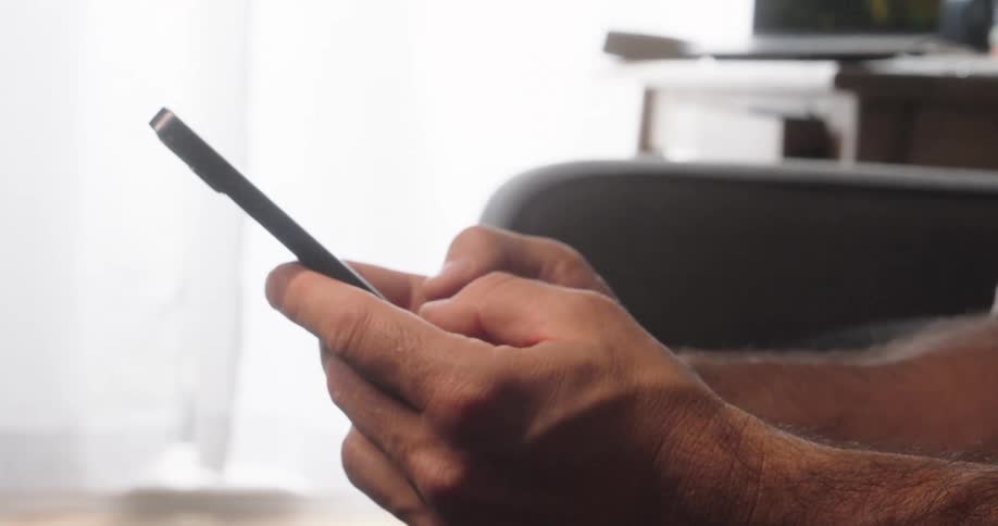 Close up of a man texting with a mobile phone while seated in a room during daytime
