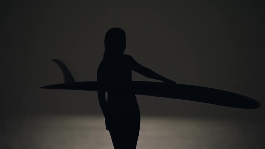 Silhouette of a surfer woman next to the sea carrying a surfboard at night under full moon light