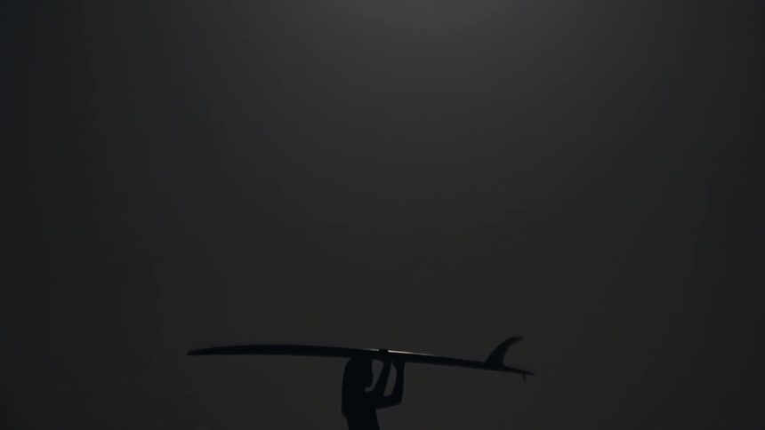 Silhouette of a surfer woman next to the sea carrying a surfboard at night under full moon light