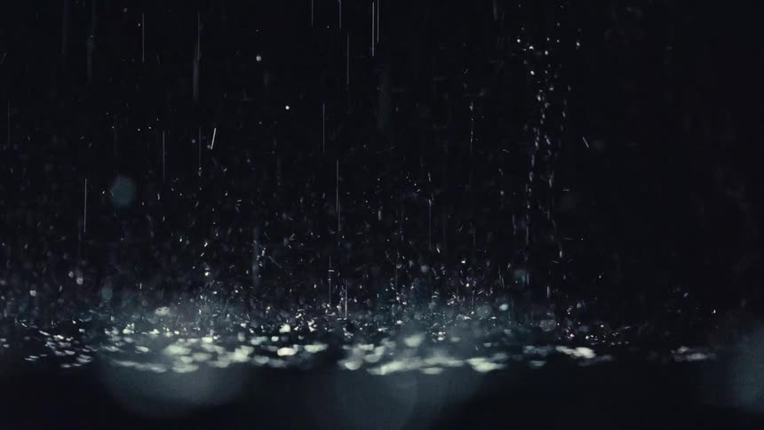 A shot of heavy rain falling and splashing onto a dark surface creating a glistening effect from a light source below