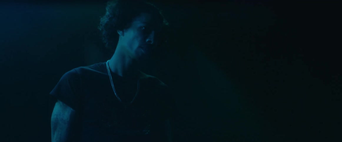 A man is standing in a dimly lit room with his back to the camera he slowly turns his head to the side revealing his profile in the light