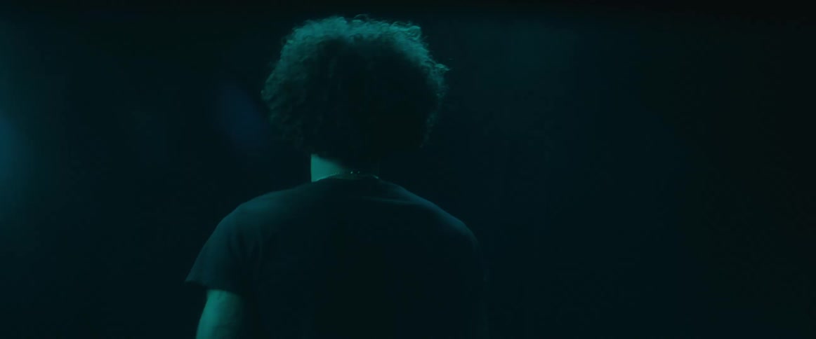 A designer walks on stage wearing a black tshirt with curly hair