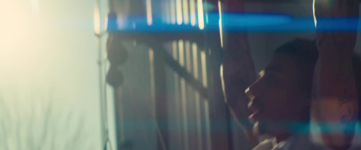 A person with tattooed arms performs pull ups with strong backlighting and a blue lens flare