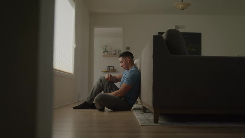 Man sitting on the floor leaning against the couch looking out the window