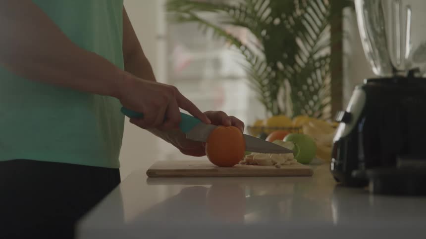 Person cutting fruits on a board next to a blender