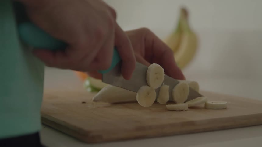 Hands slicing a banana into rounds on a wooden cutting board