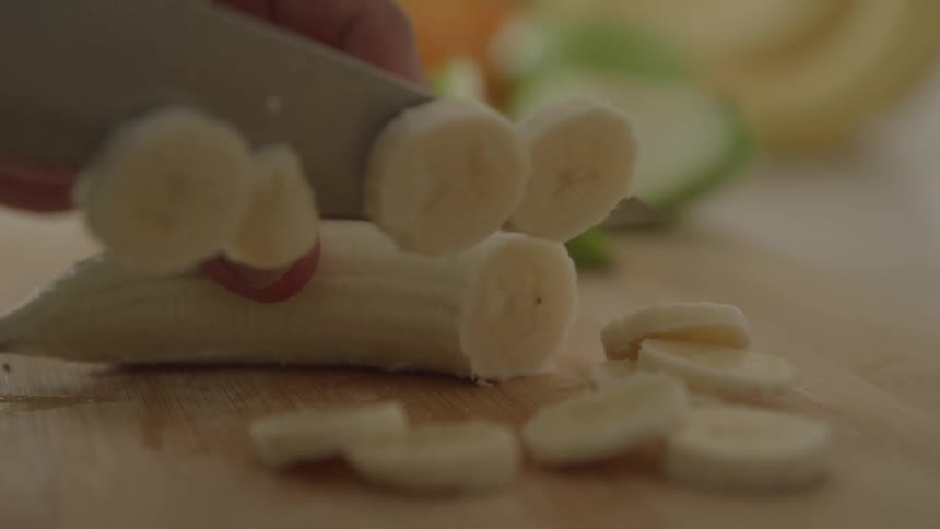 Knife slicing banana into rounds on a wooden cutting board