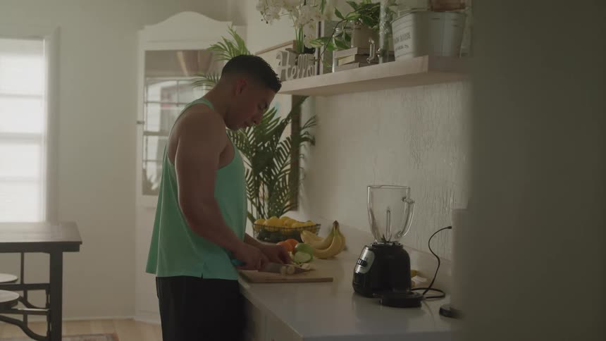 The man is cutting fruit to put in a blender