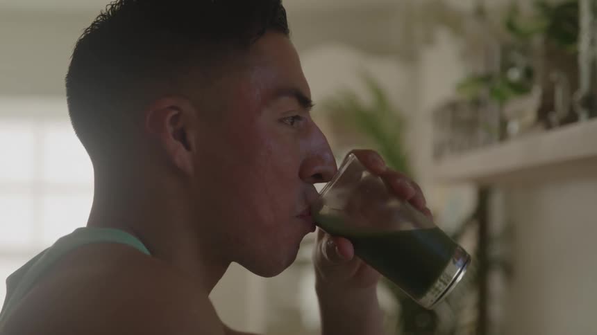 Man drinking a green juice from a glass