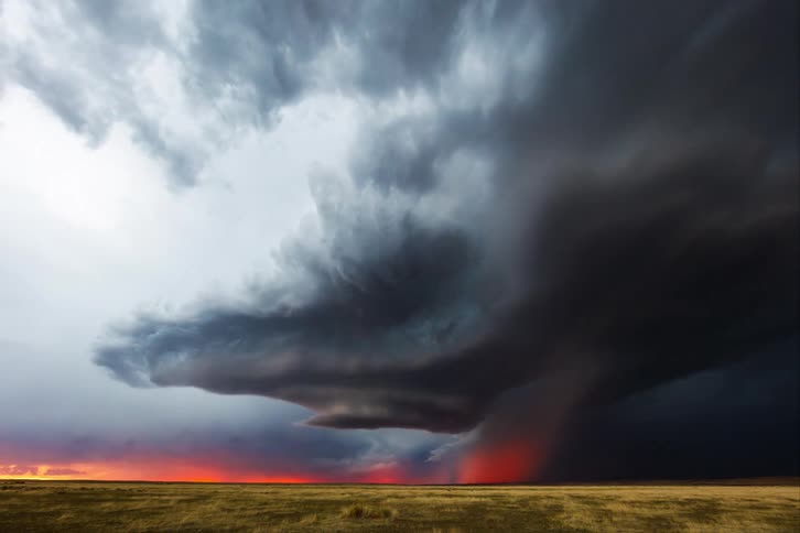 Dark storm clouds swirl over open plains at sunset