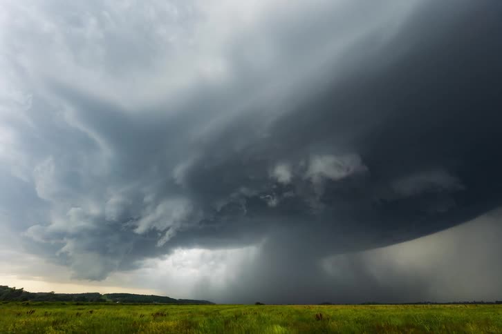 A tornado swirls beneath dark storm clouds over grasslands