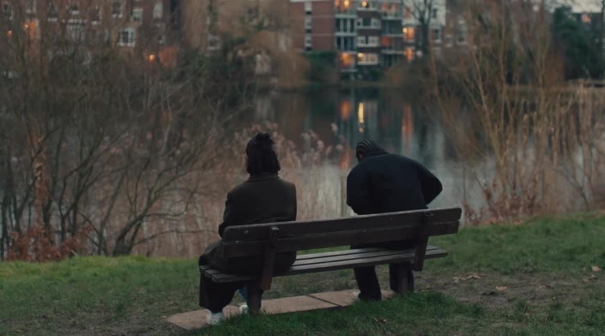 Man sitting on a bench facing a lake next to a woman