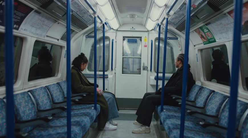 Two individuals sit across from each other on a subway train