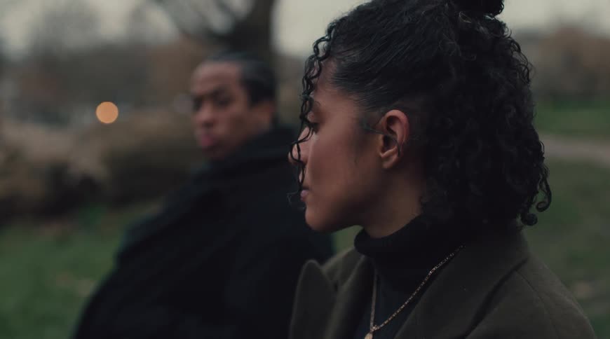 Thoughtful woman in an outdoor setting and a man watching beside her