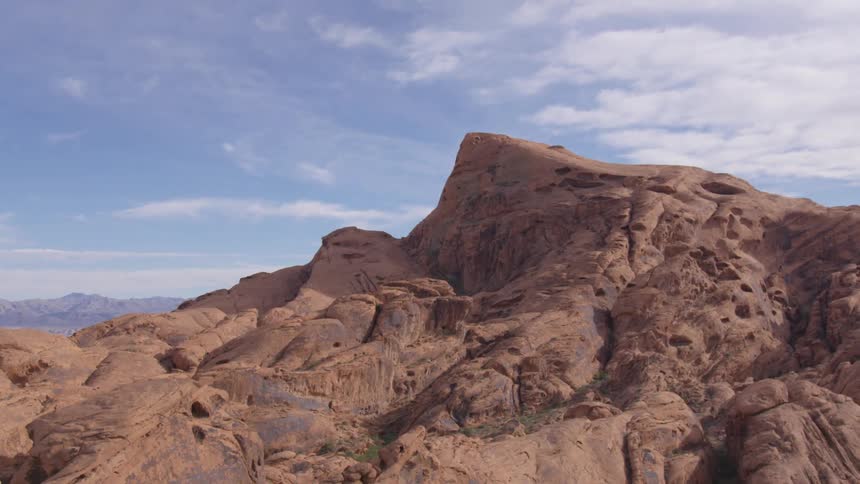 An aerial view captures the majestic red rock formations of a desert landscape under a partially cloudy blue sky
