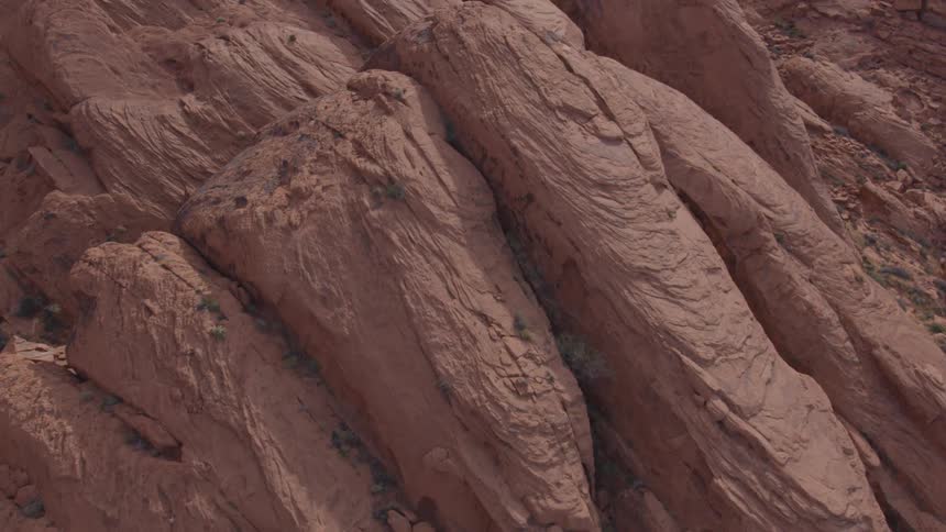 The camera slowly tilts down a massive textured rock face revealing layers of deep red and brown sediment the rock is sculpted with smooth flowing curves and distinct striations hinting at years of natural erosion