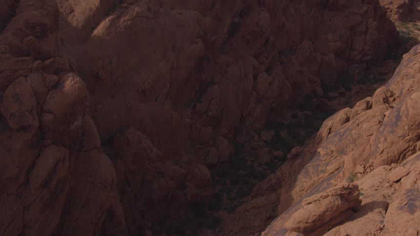 Towering reddishbrown rock formations rise on either side of a narrow shadowed canyon