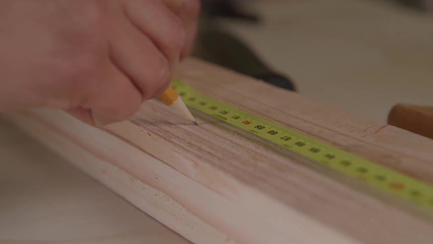 A person measures a piece of wood with a tape measure