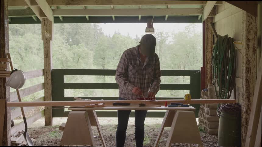 Person measuring and marking a wooden plank in a workshop
