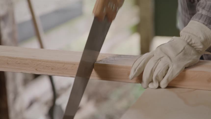 Person sawing a wooden plank with a hand saw
