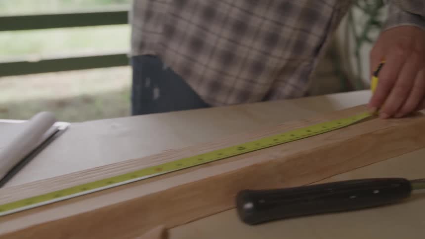 Person measuring and marking a piece of wood with a tape measure and pencil